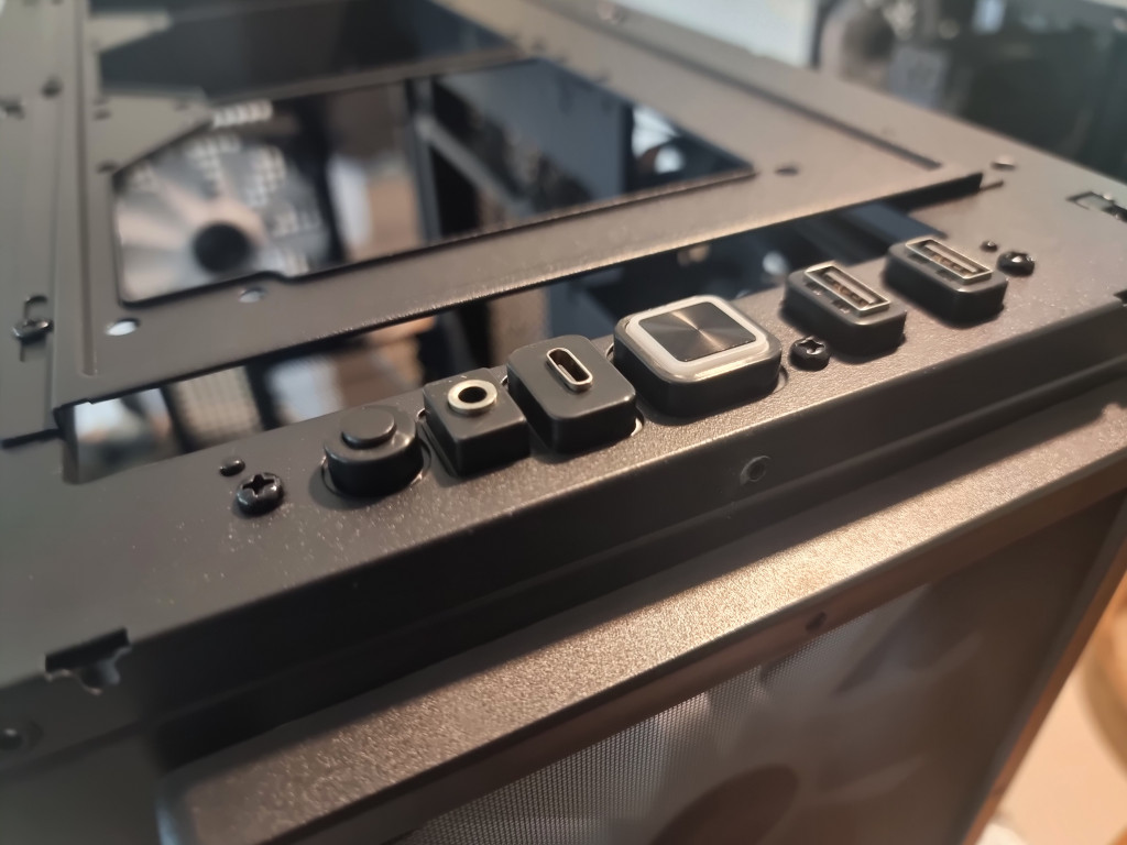 photo showing a close up of the i/o header on the top of the pc case. The metal panel has been removed and the buttons and sockets sit proud on the black frame.