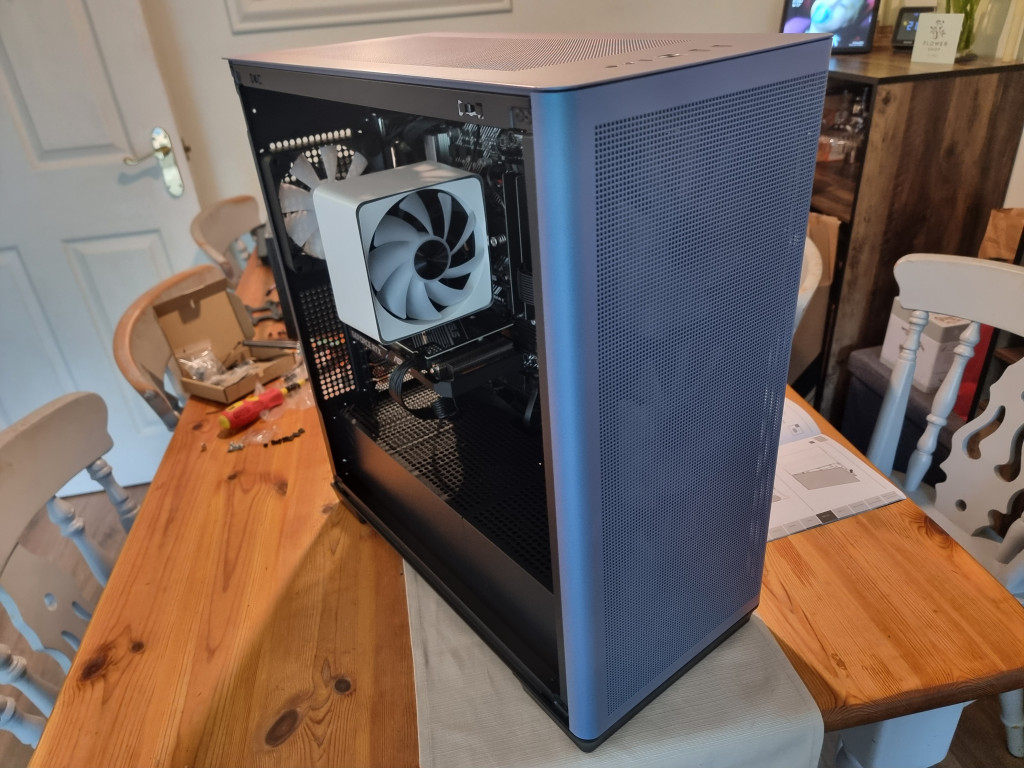 photo showing the finished case sitting on a wooden table with the glass side removed. Inside you can see the white cpu cooler and one of the FP1 exhaust fans in the distance.